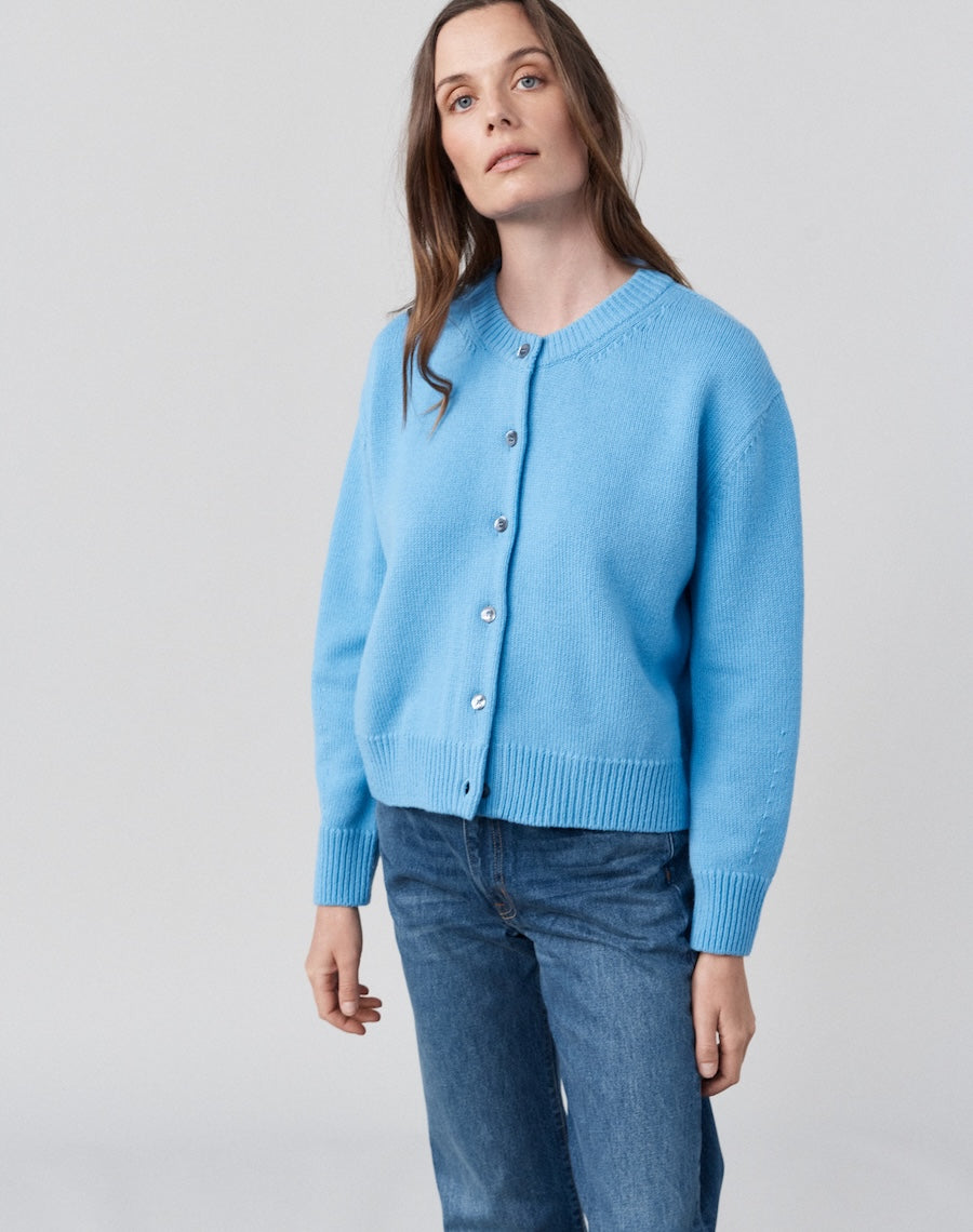 Woman wearing a light blue cardigan and jeans on a plain background