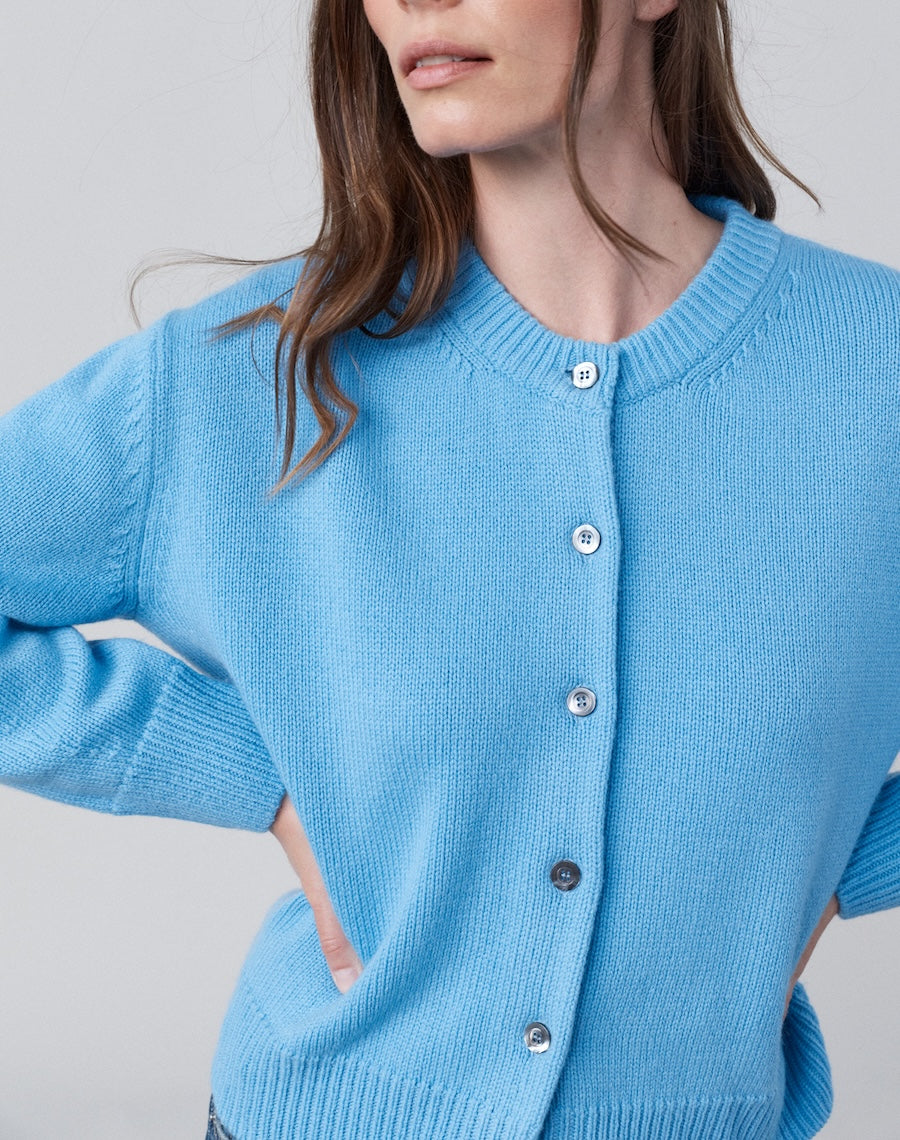 Person wearing a blue cardigan with a plain background